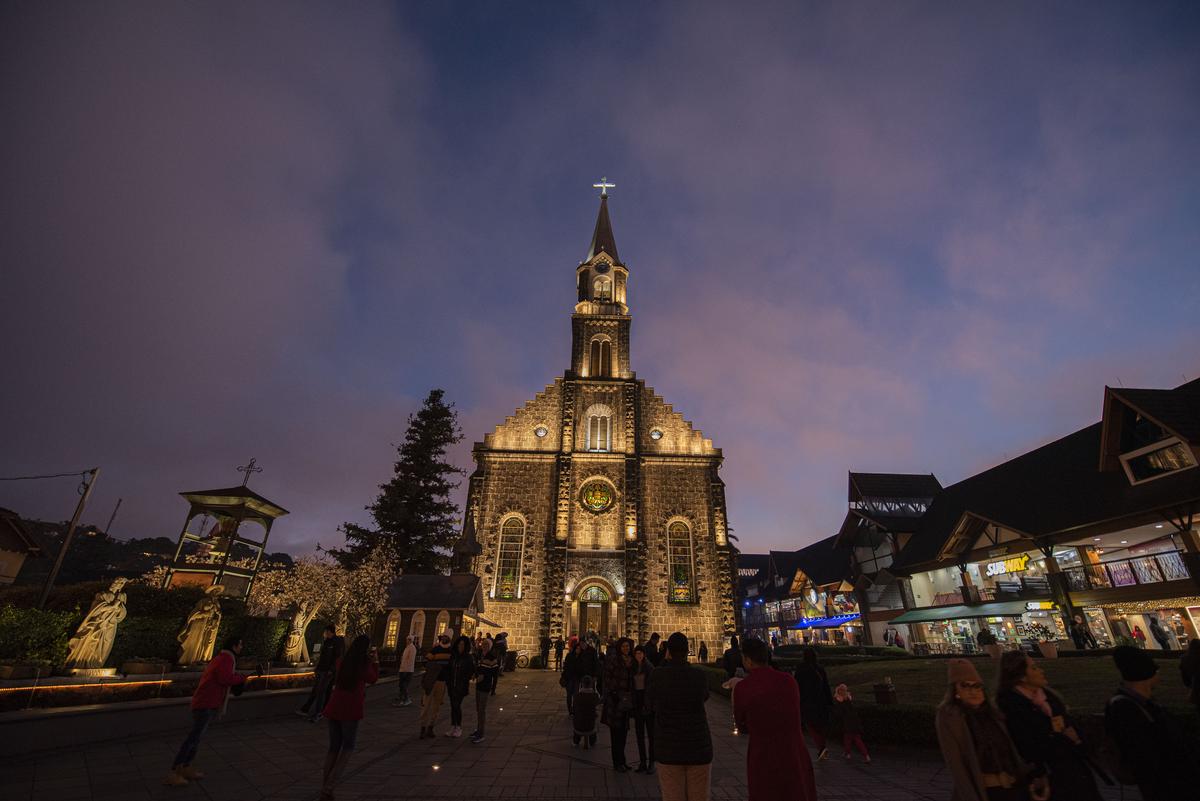 Casal sorridente caminhando por uma rua de paralelepípedos com cafés pitorescos e árvores floridas, exemplificando a vida na cidade mais charmosa do Brasil.